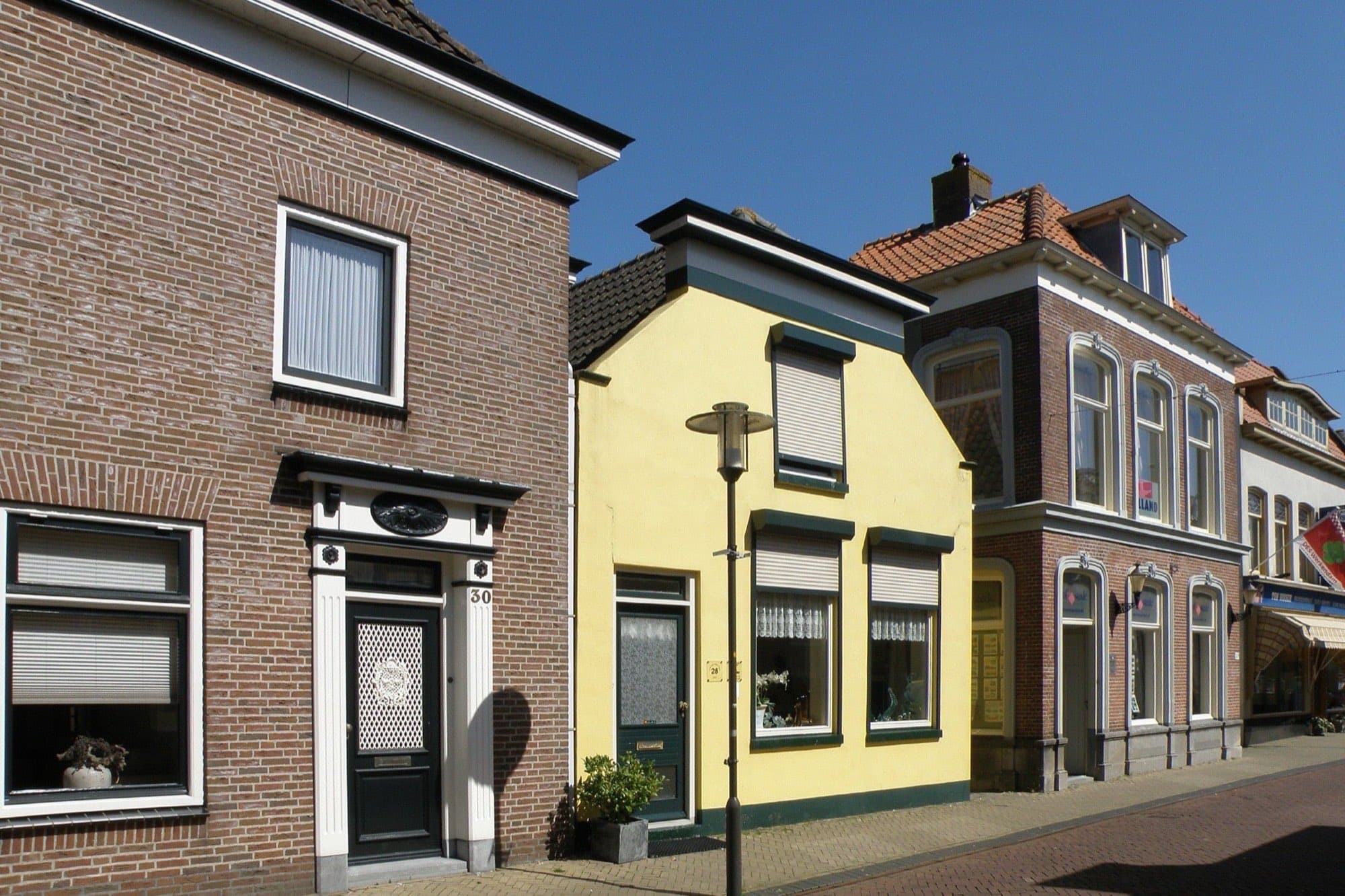 Rij woonhuizen aan de Hoogstraat in Werkendam, gemeente Altena, met een geel geschilderd hoekpand en bakstenen huizen met pannendaken onder een blauwe lucht.