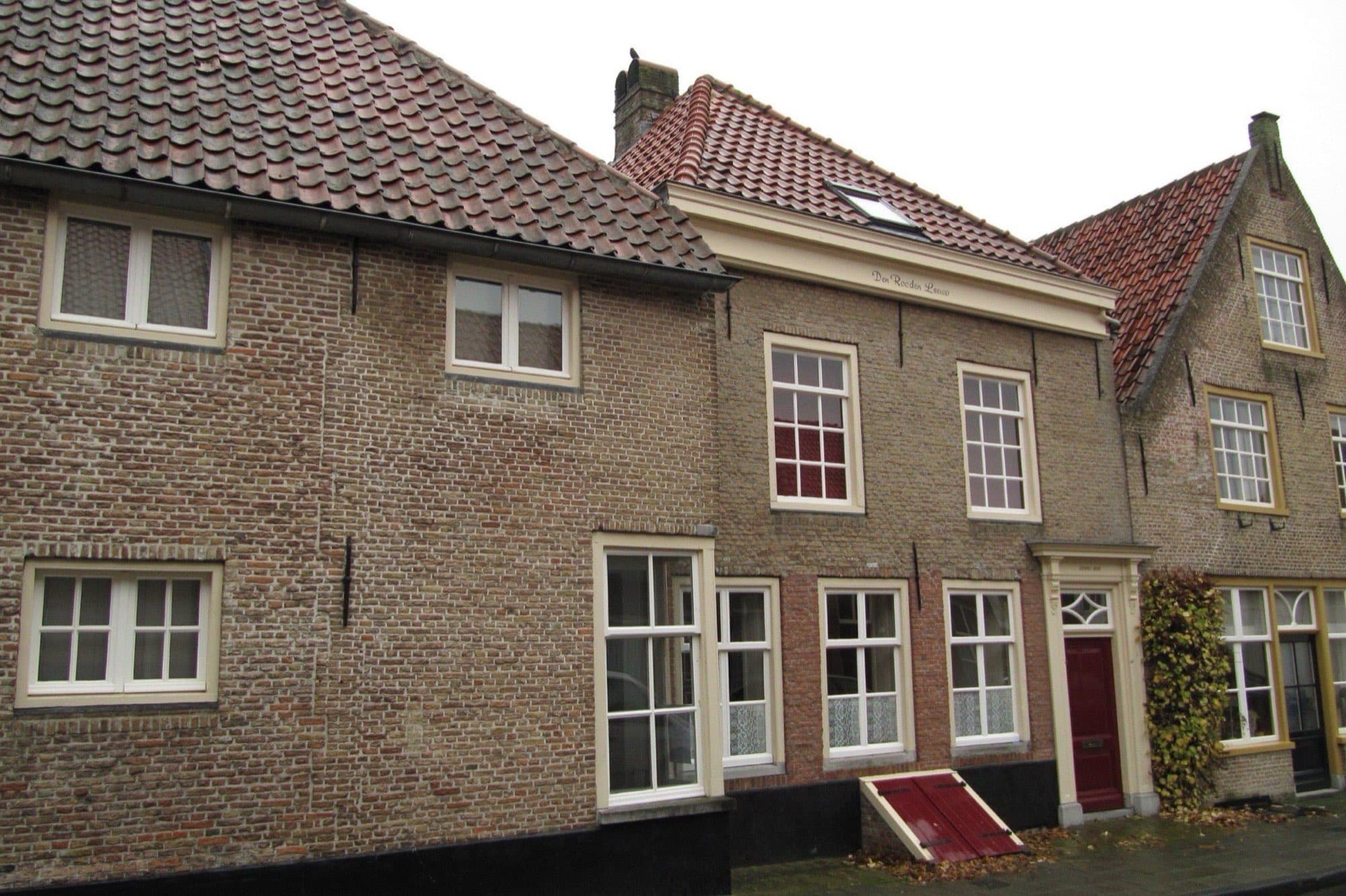 Lage bakstenen woonhuizen met witte kozijnen, een rode voordeur en pannendaken aan de Dubbelstraat in de binnenstad van Bergen op Zoom.