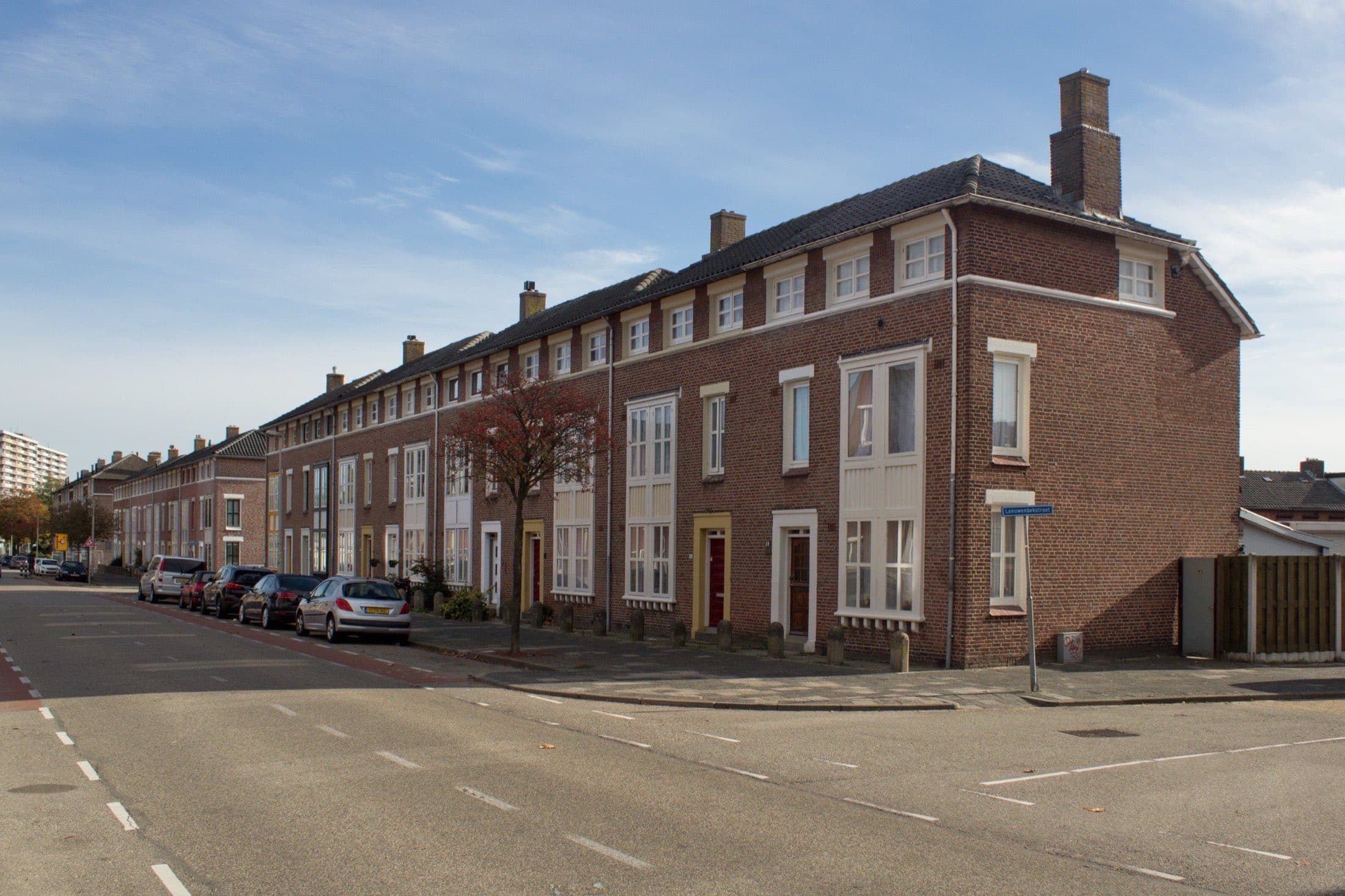 Lange rij bakstenen woningen van twee lagen in Bossche Schoolstijl uit 1950 aan de Gentiaanstraat in Bergen op Zoom, onder een blauwe lucht.