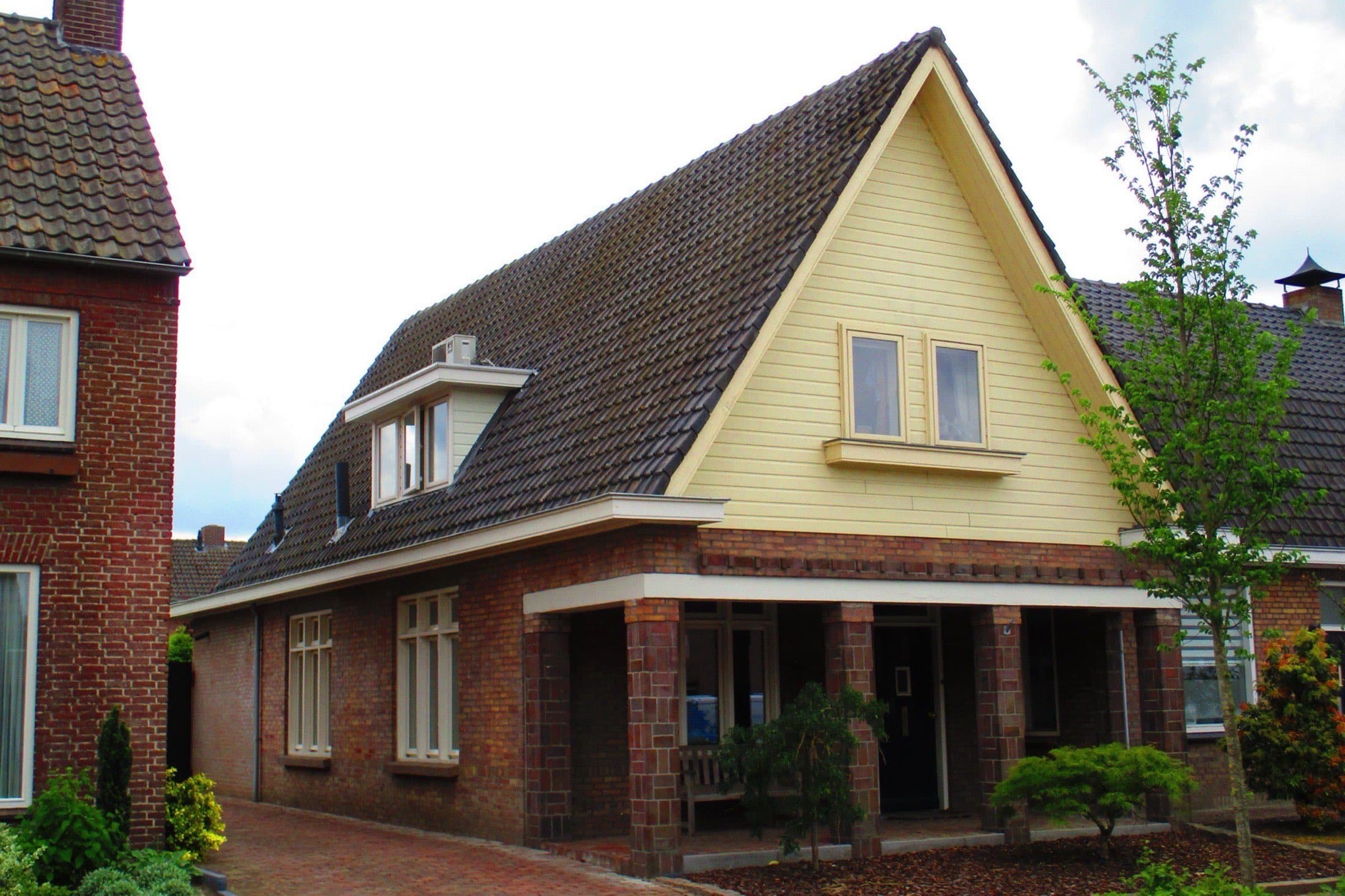 Bakstenen woonhuis met een hoog pannendak, een gele houten puntgevel en een overdekte veranda op bakstenen pijlers aan de Hoofdstraat in Heeswijk-Dinther, gemeente Bernheze.