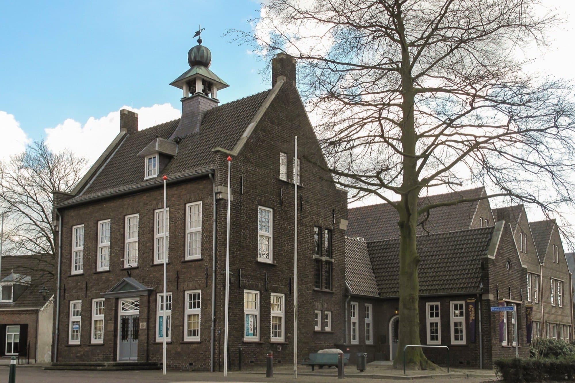 Bakstenen monumentaal pand met witte kozijnen, een dakruiter met klokje en een hoog pannendak in het centrum van Nistelrode, gemeente Bernheze.