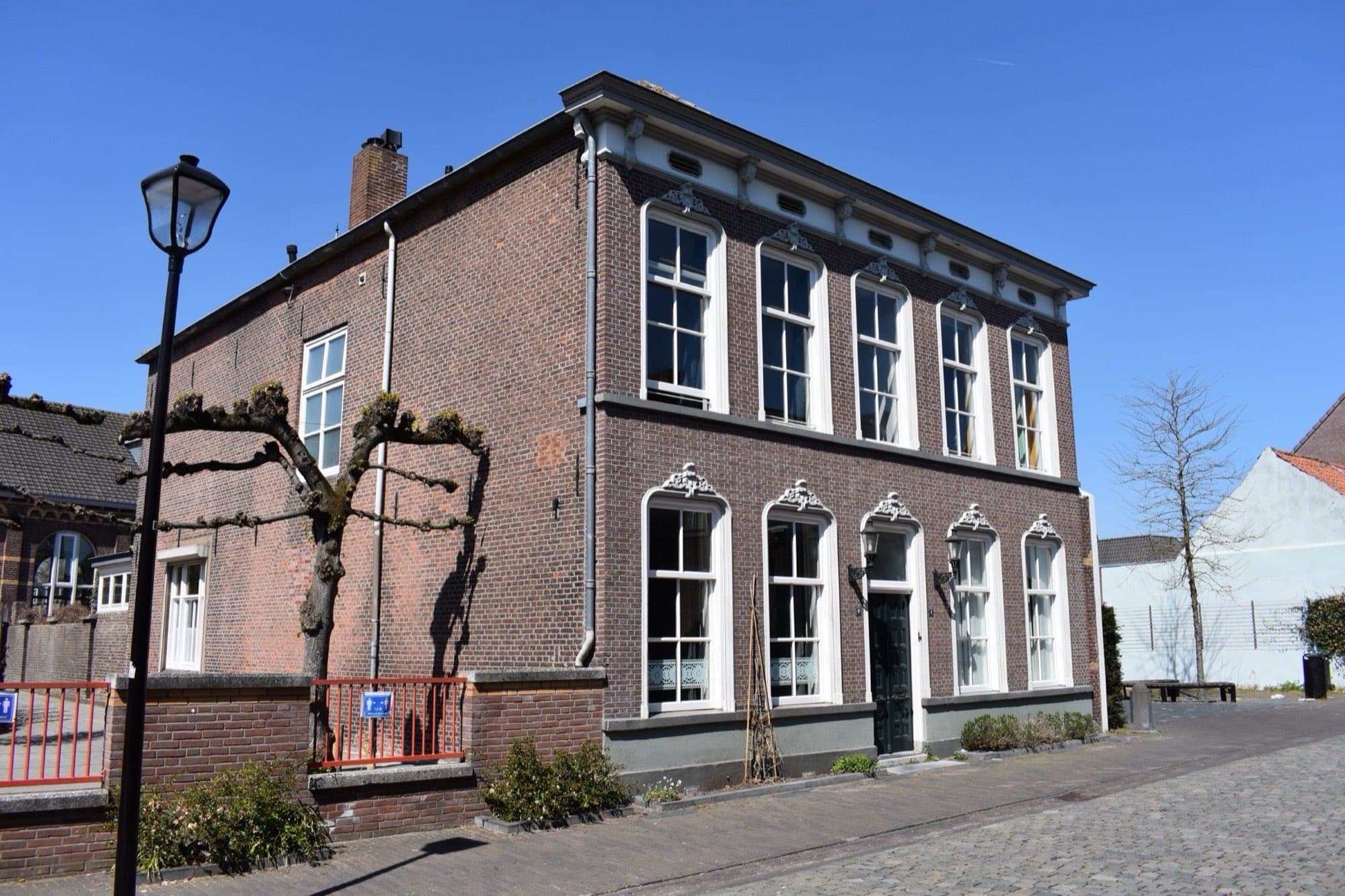 Bakstenen herenhuis van twee lagen met witte kozijnen en een lantaarnpaal ervoor aan de Burgakker in Boxtel, onder een strakblauwe lucht.