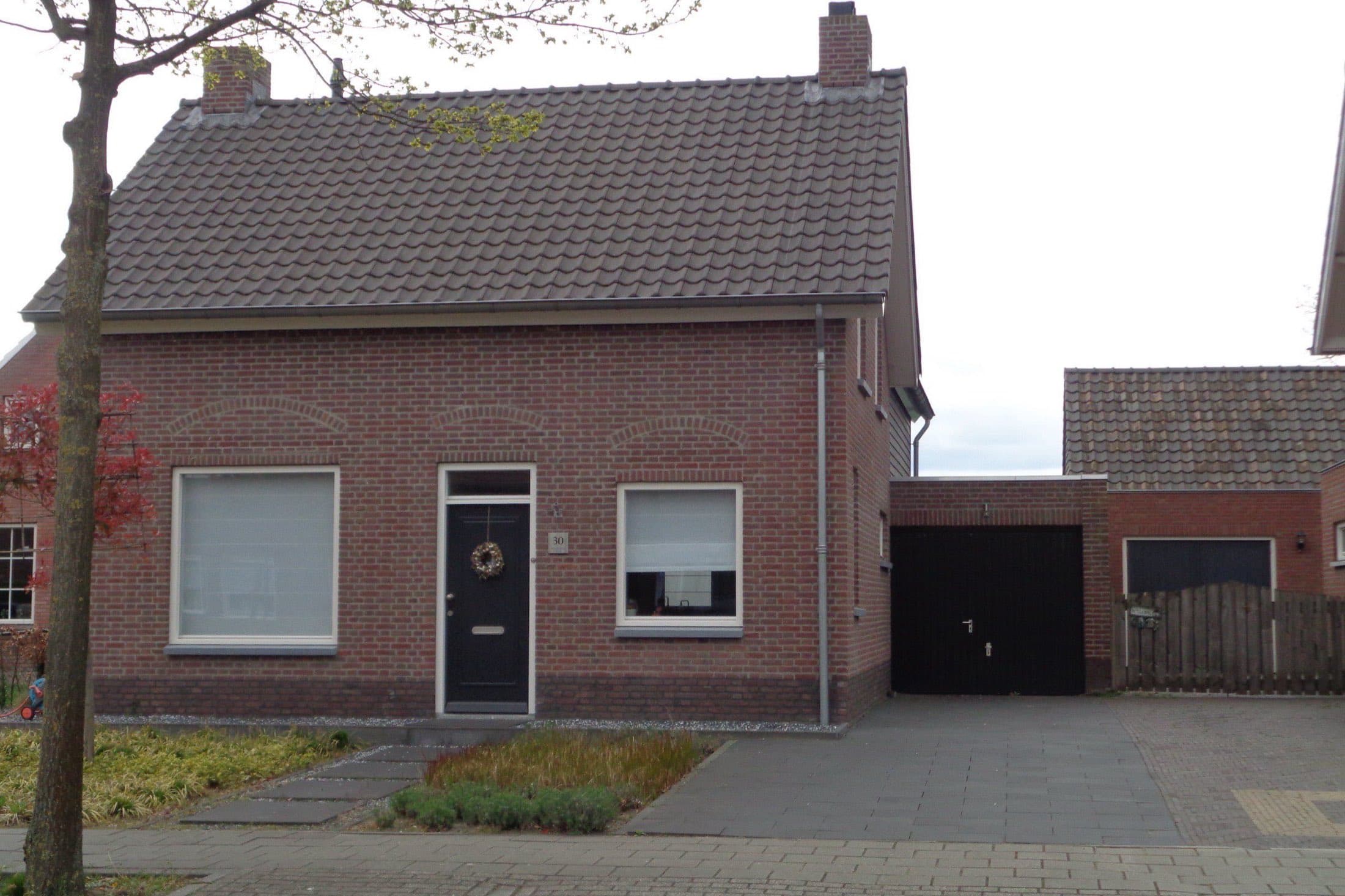 Vrijstaand bakstenen woonhuis met pannendak, witte kozijnen en een garage aan de Zandstraat in Liessel, gemeente Deurne.