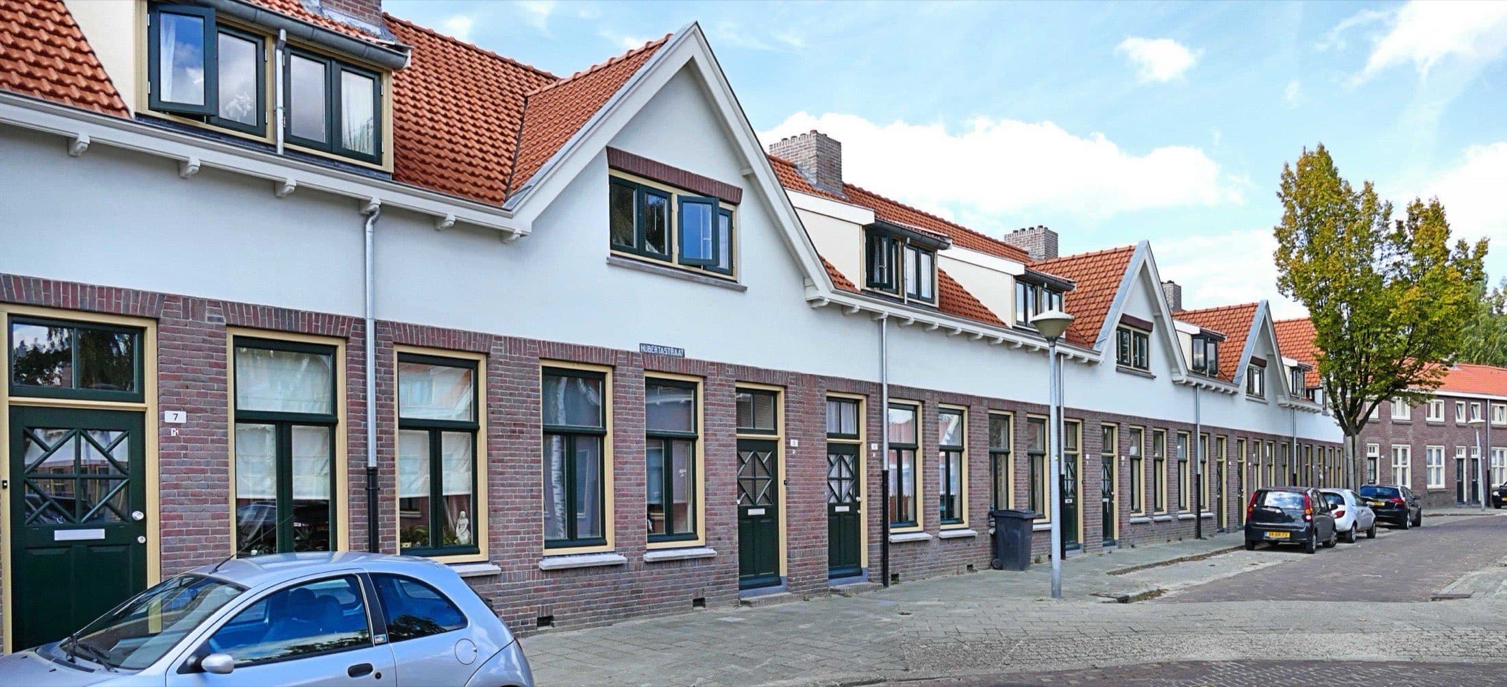 Witte en bakstenen woningen met oranje pannendaken aan de Hulstlaan in Philipsdorp, Eindhoven, onder een strakblauwe lucht.