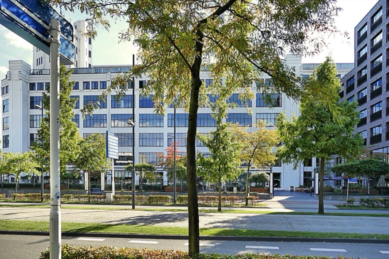 Wit voormalig Philips-kantoorgebouw met grote raampartijen achter jonge bomen langs een brede laan in Eindhoven.