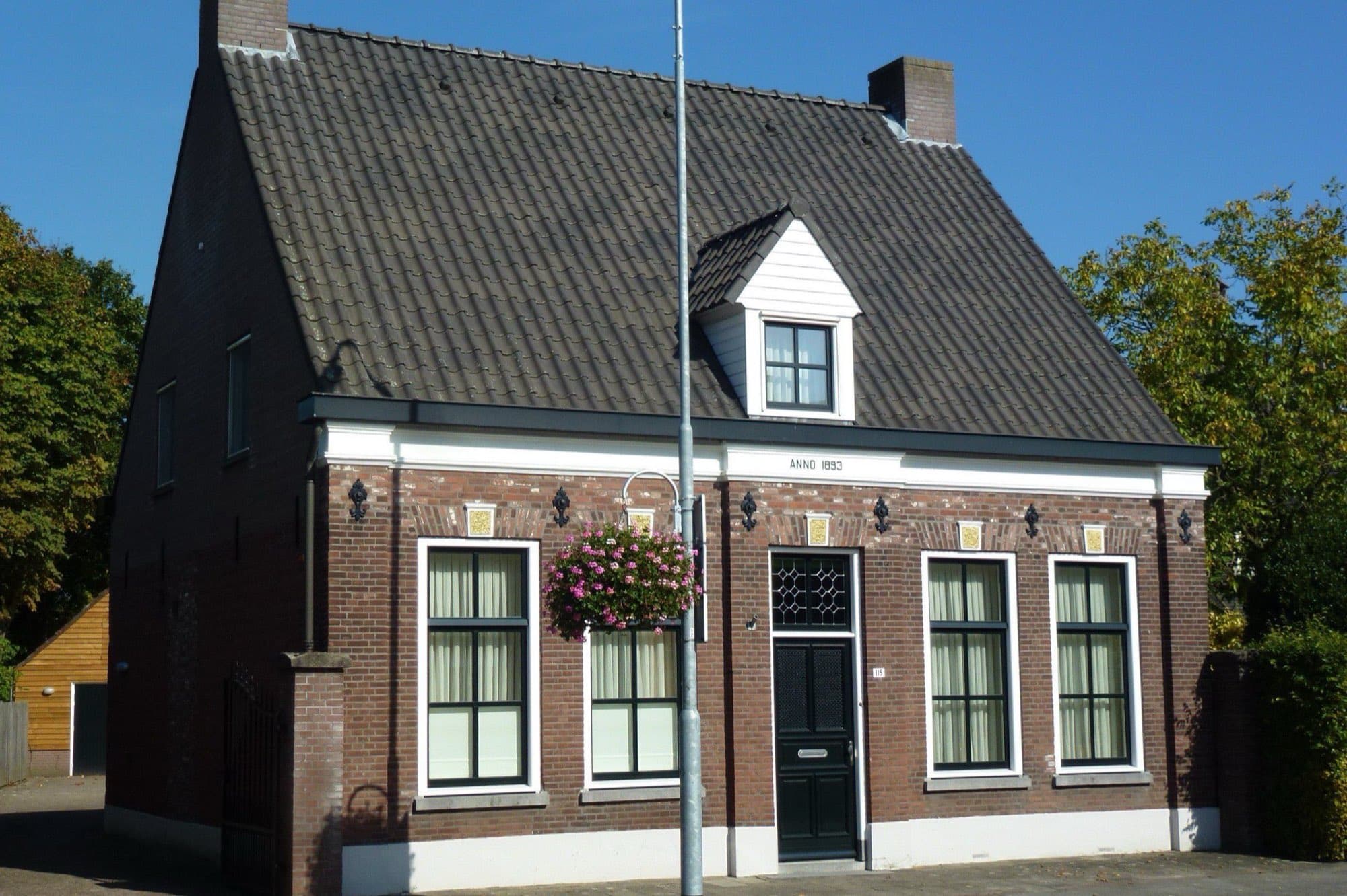 Bakstenen woonhuis met zwart pannendak, witte kozijnen en een dakkapel aan de Dorpsstraat in Mierlo, gemeente Geldrop-Mierlo, onder een strakblauwe lucht.