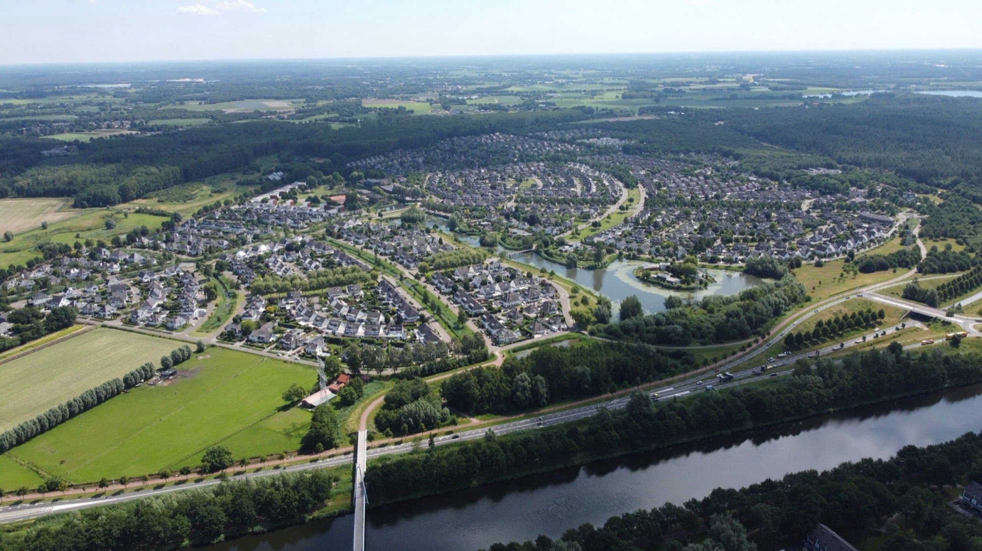 Luchtfoto van de woonwijk Dierdonk in Helmond met rijtjeswoningen, een vijver en groen, en op de voorgrond een kanaal en weilanden.
