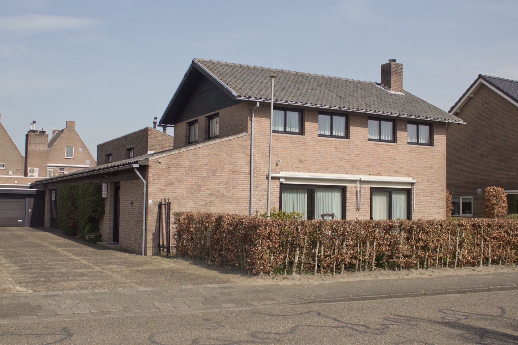 Twee-onder-een-kapwoningen van bruine baksteen met pannendaken en hagen aan de Van Hoogendorpstraat in Drunen, gemeente Heusden.