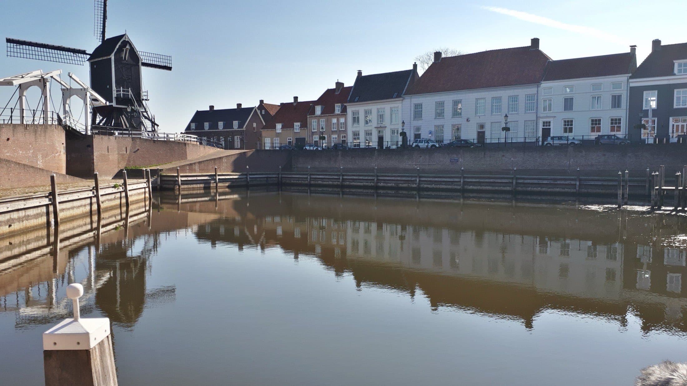 De lege binnenhaven van vestingstad Heusden met een rij oude huizen langs de kade en links een windmolen op de vestingwal, gespiegeld in het water.