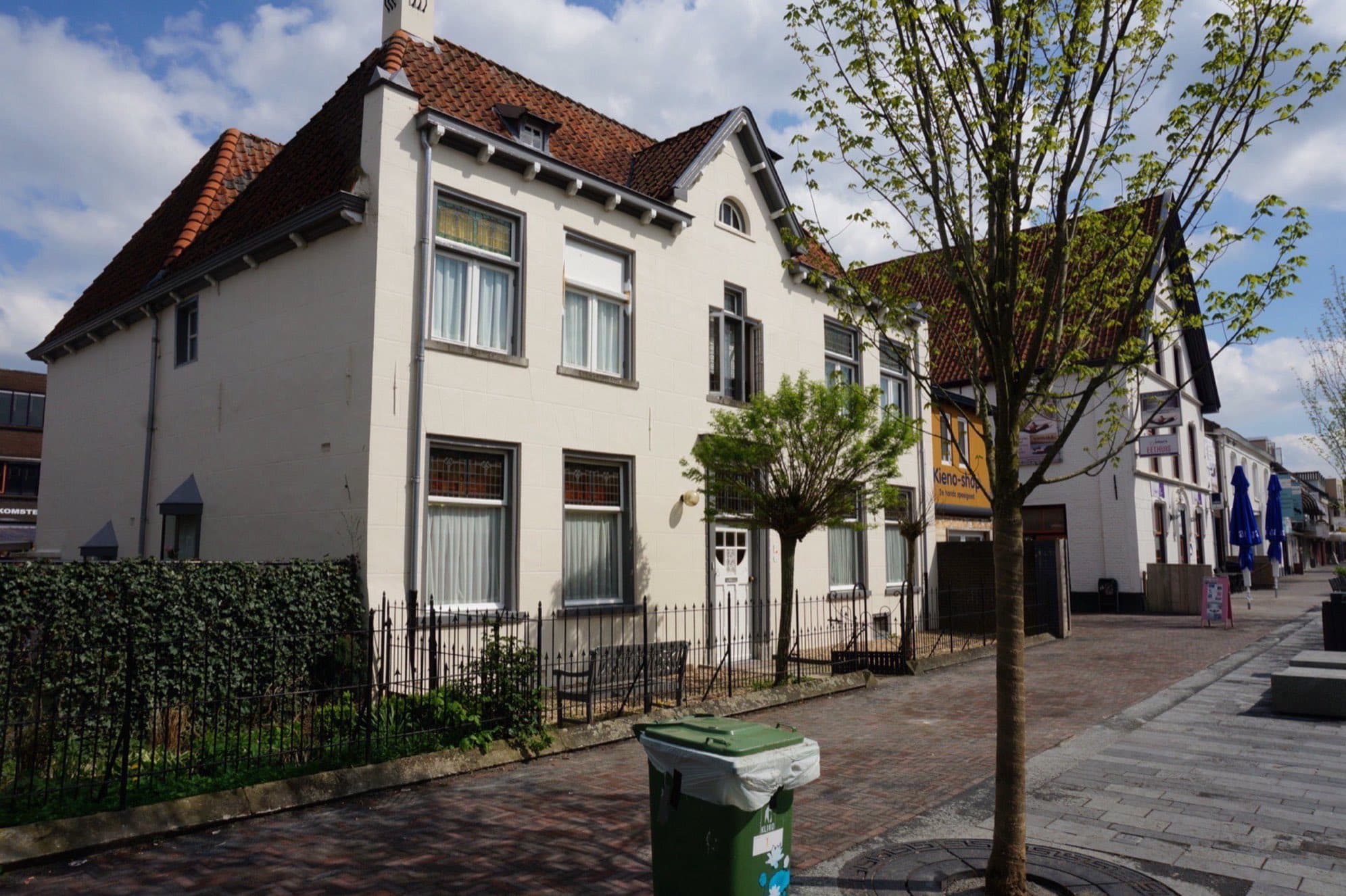 Twee witgepleisterde woonhuizen met pannendaken en groene luiken op de hoek van de Grotestraat in Cuijk, gemeente Land van Cuijk, met een jonge straatboom ervoor.