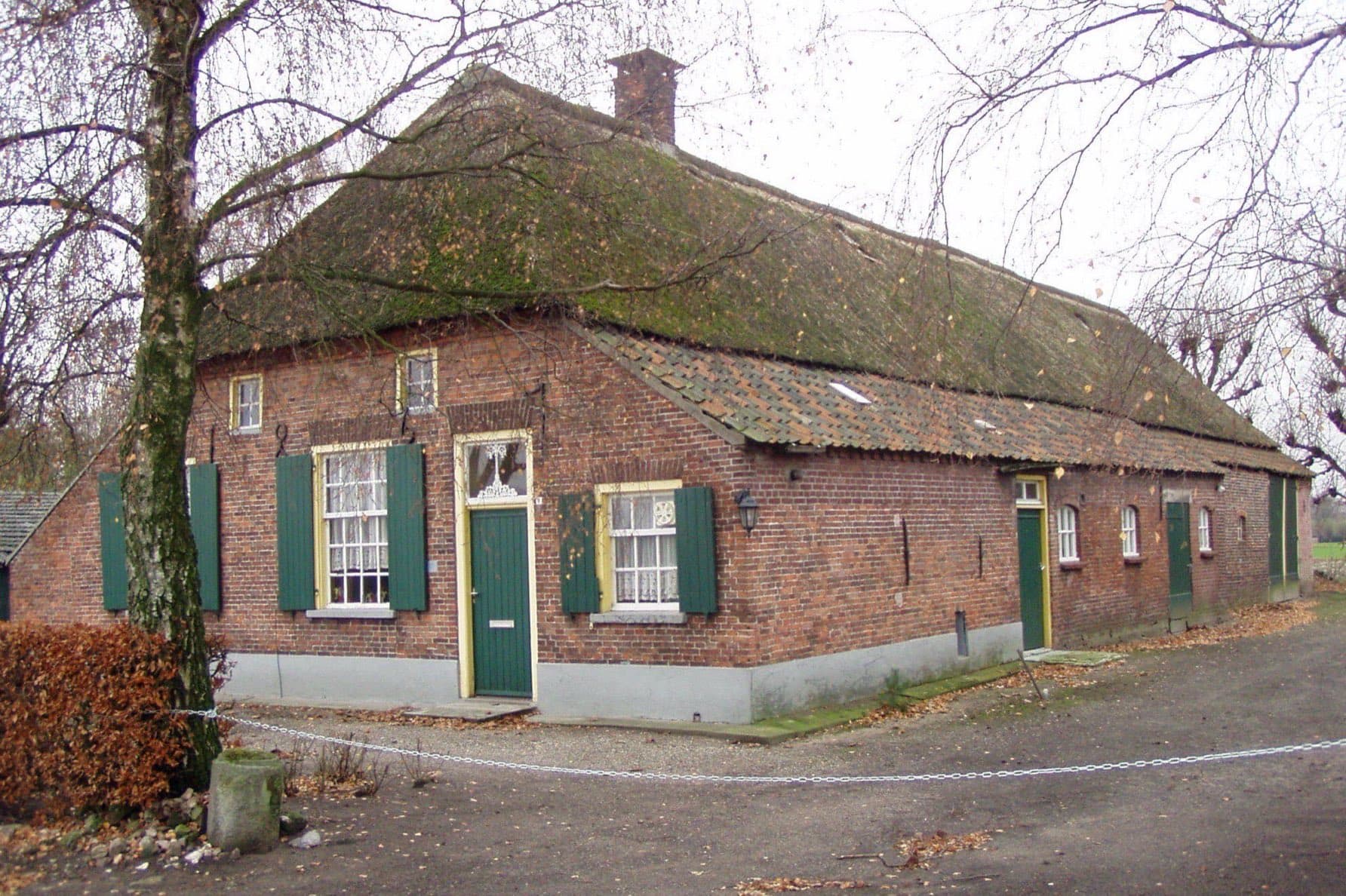 Rietgedekte langgevelboerderij met groene luiken en een gele voordeur aan de Hofsteeweg in Uden, gemeente Maashorst, tussen kale bomen in de winter.
