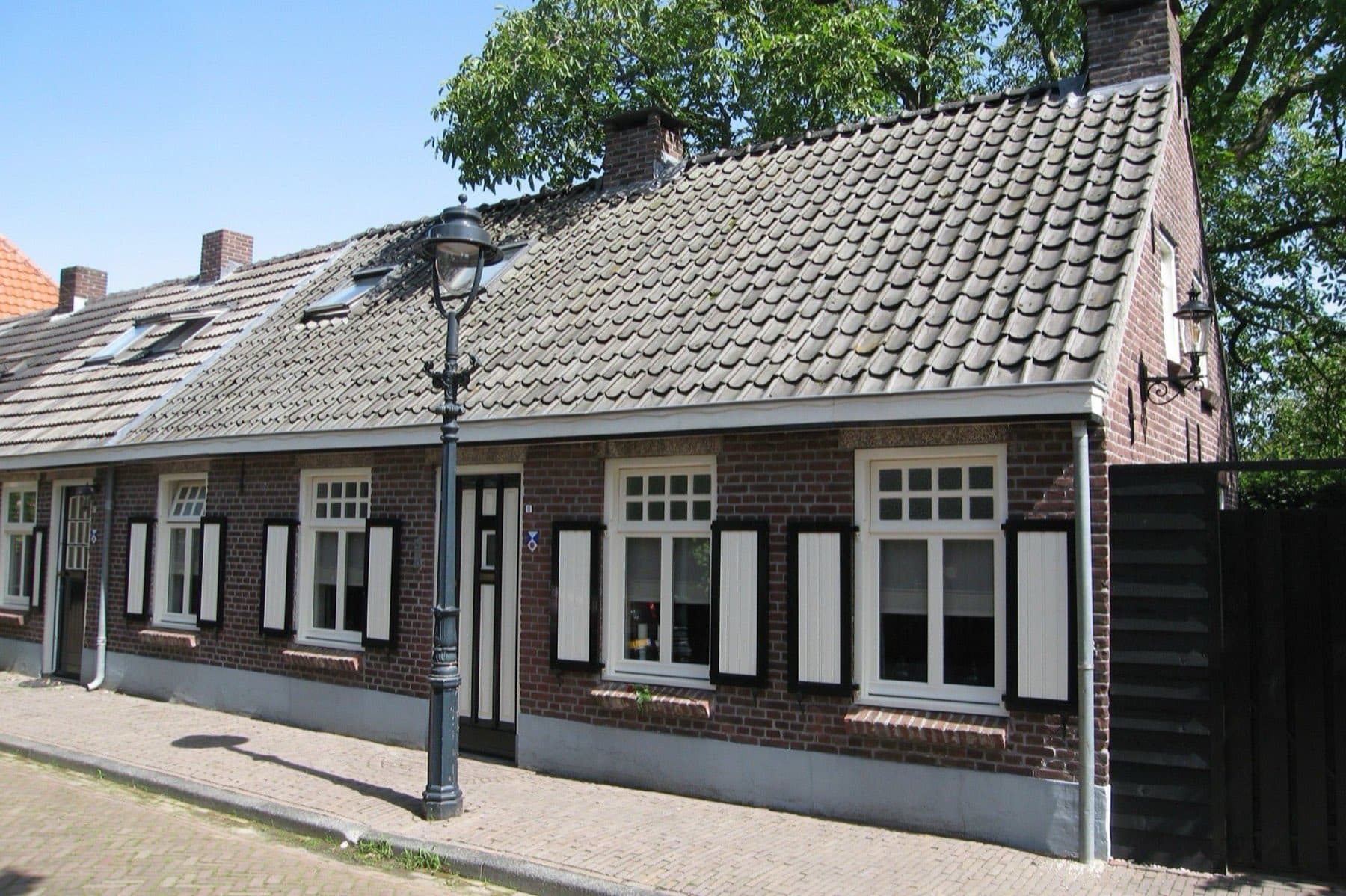 Rij lage bakstenen woningen met pannendaken, witte kozijnen, wit-zwarte luiken en een ouderwetse lantaarnpaal aan de Vorstenburg in Uden, gemeente Maashorst.