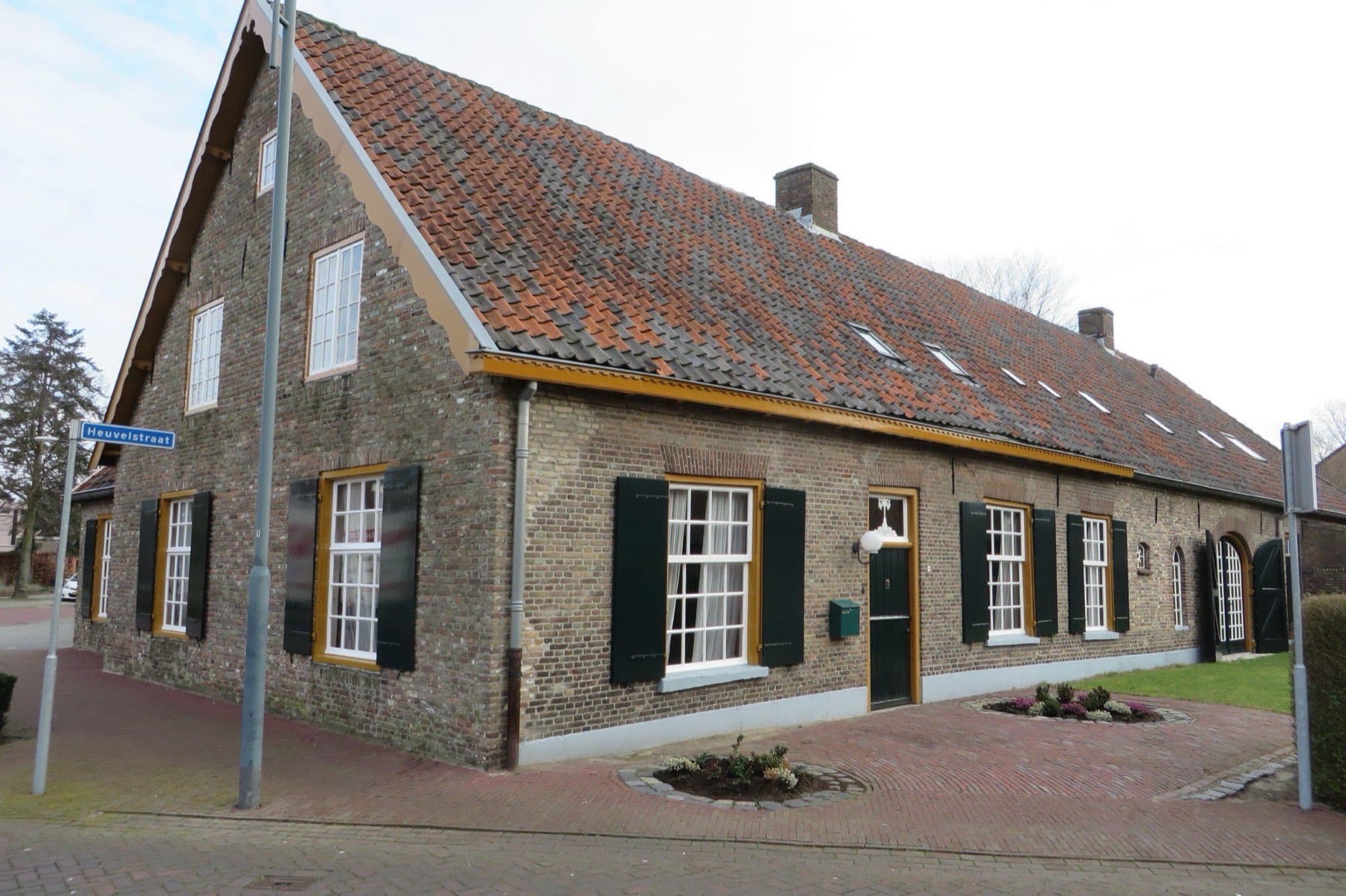 Bakstenen langgevelboerderij met een oranje pannendak, groene luiken en gele kozijnen aan de Hoofdstraat in Veghel, gemeente Meierijstad.