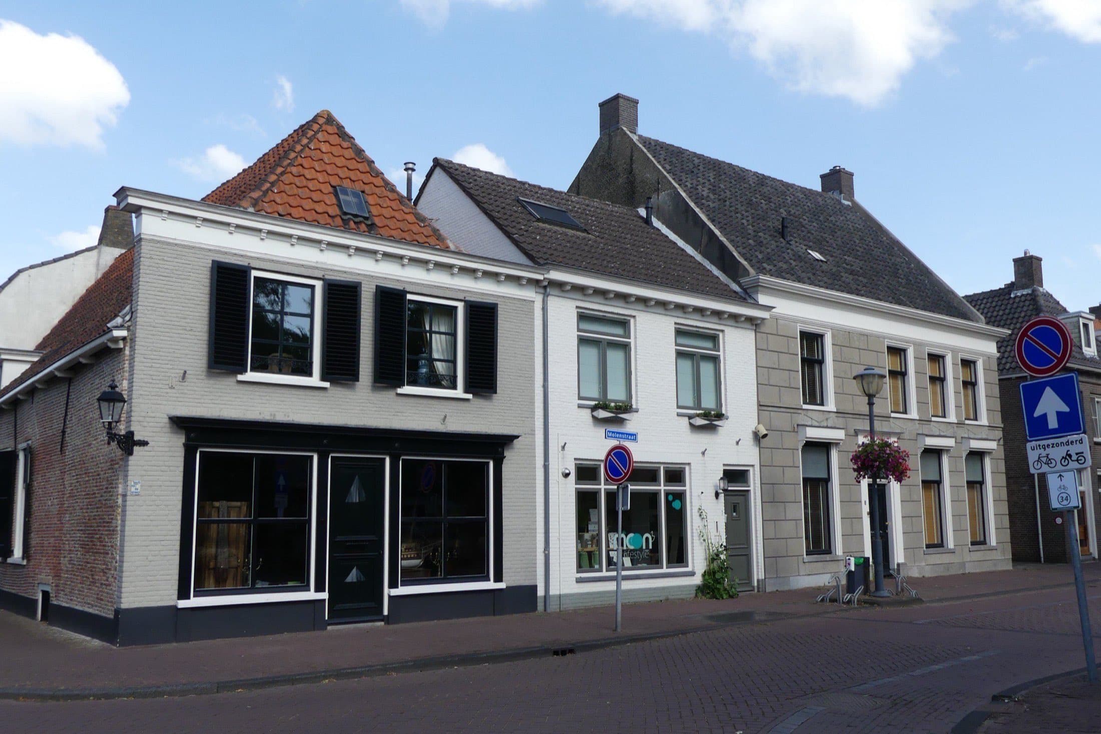Rij oude woonhuizen met lichte gevels en pannendaken aan de Molenstraat in Klundert, gemeente Moerdijk, onder een blauwe lucht met wolken.