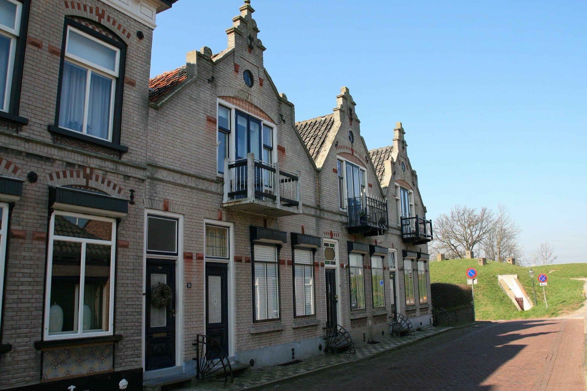 Rij bakstenen dijkwoningen met trapgevels en witte kozijnen aan de Raadhuisstraat in vestingstadje Willemstad, gemeente Moerdijk, onder een blauwe lucht.