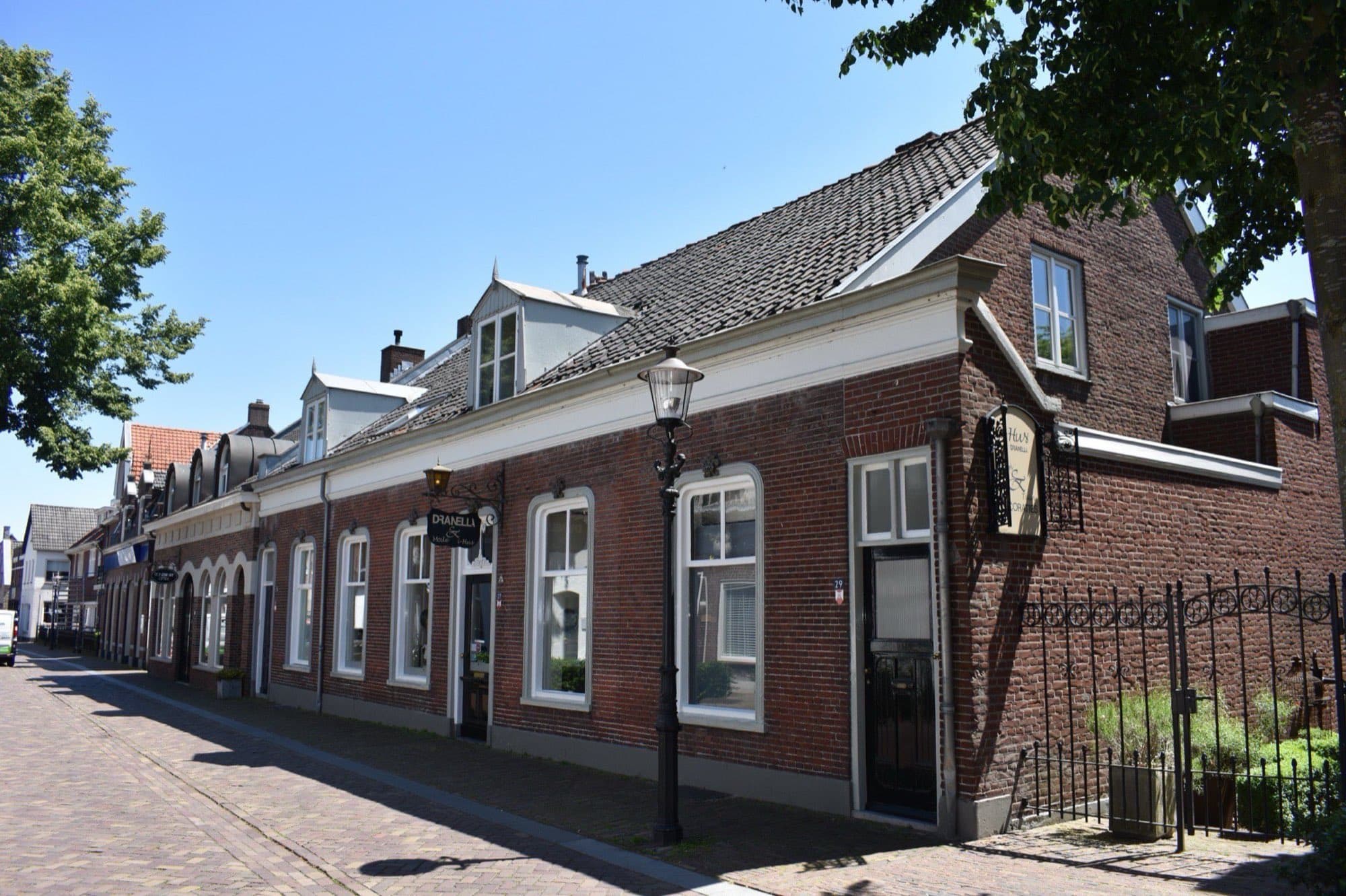Rij oude bakstenen woningen met witte kozijnen en dakkapellen aan de Kerkstraat in Oisterwijk, onder een blauwe lucht.