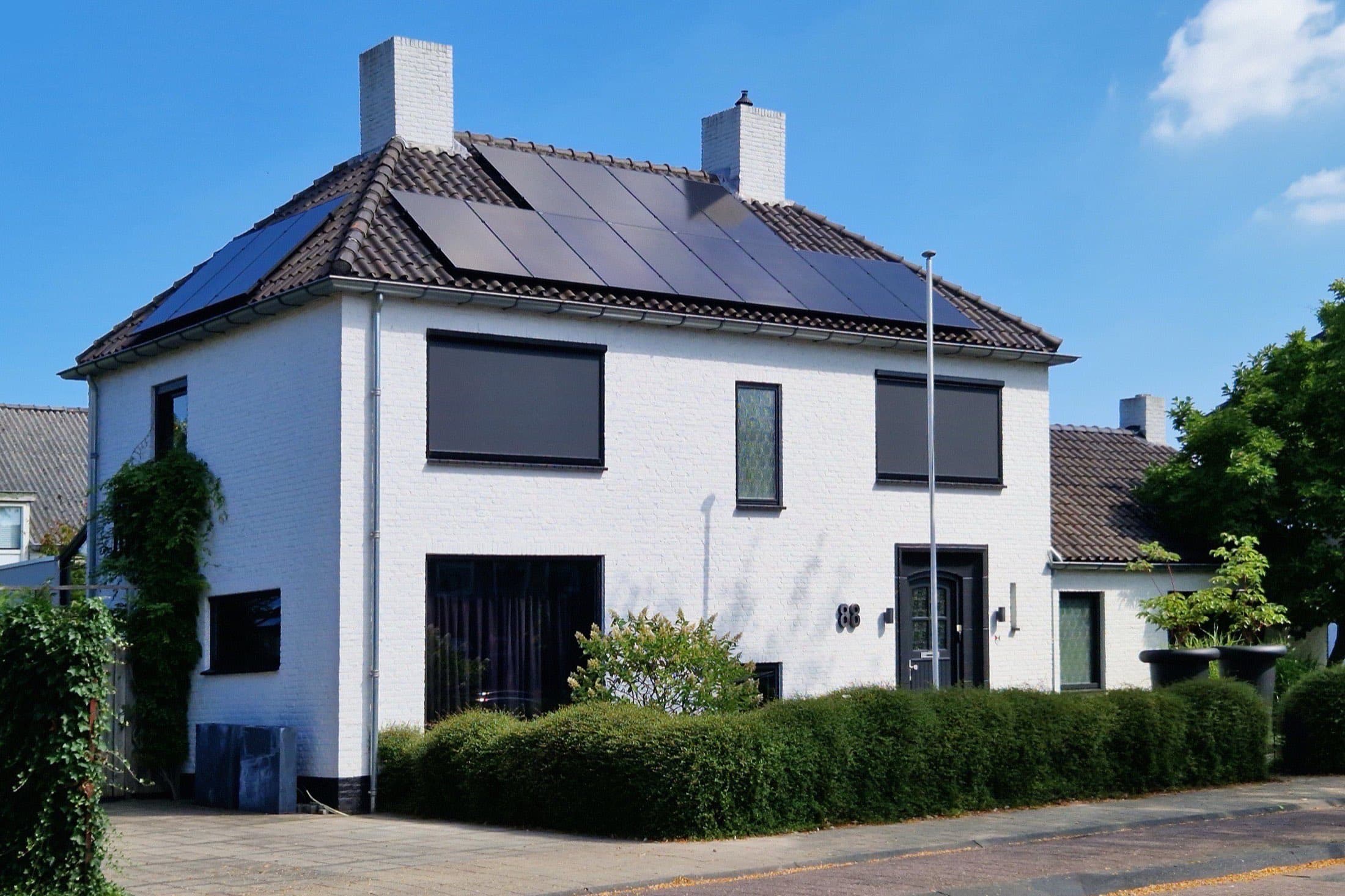 Wit vrijstaand woonhuis met zonnepanelen op het pannendak en een groene haag aan de Wilhelminalaan in Oosterhout, onder een blauwe lucht.