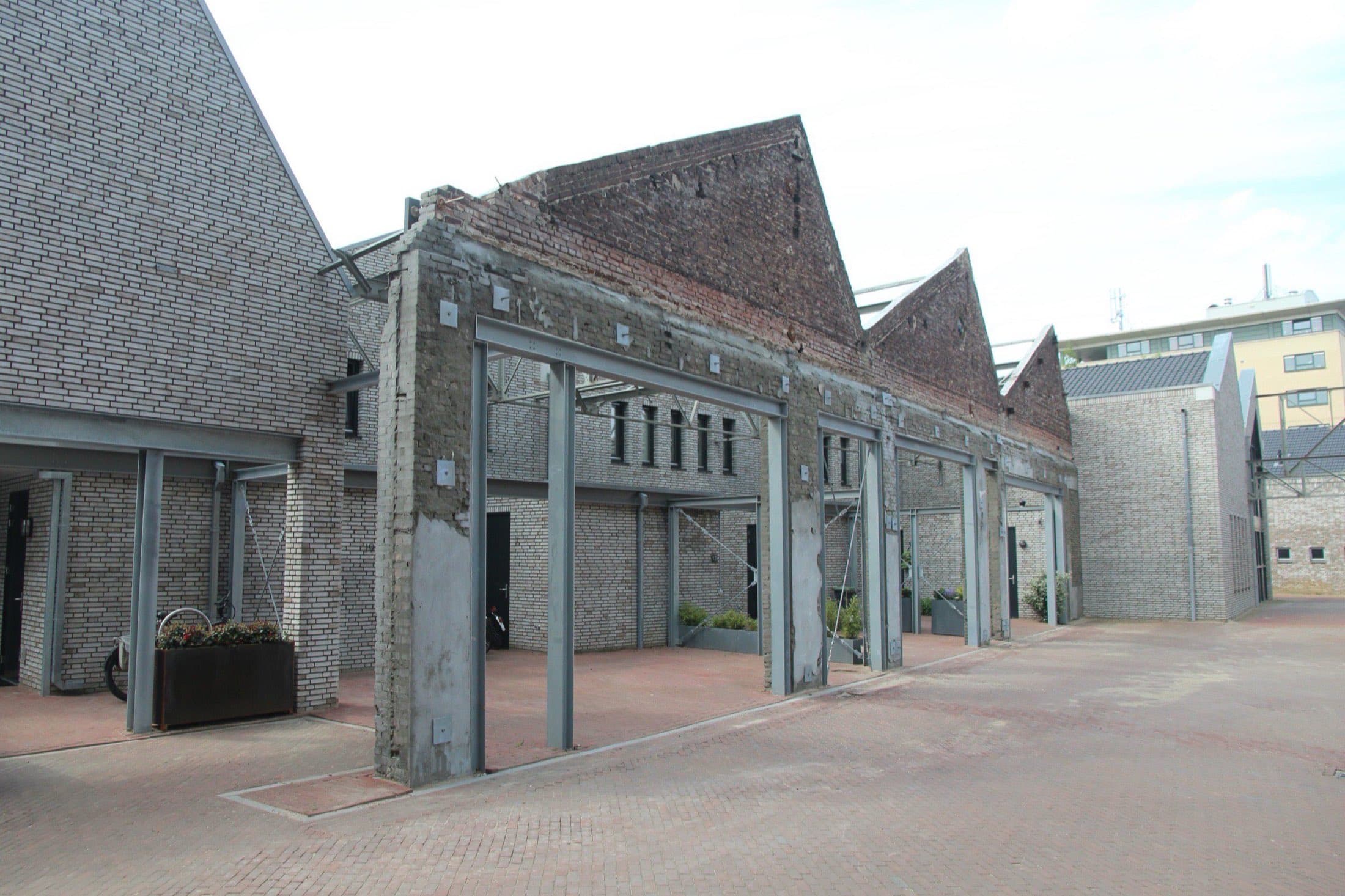 Moderne woningen van lichte baksteen met puntdaken op het voormalige Bergoss-terrein aan de Koningsloper in Oss, met een bewaarde stalen fabrieksconstructie.