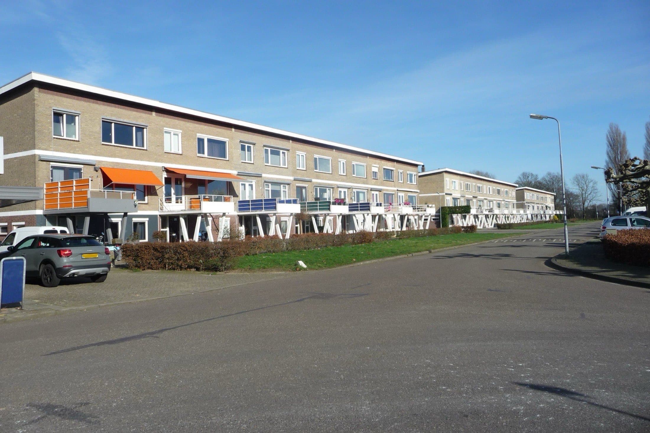 Rij portiekflats van drie lagen met balkons en oranje zonneschermen aan de Rijnstraat in de Aawijk in 's-Hertogenbosch, op een zonnige winterdag.