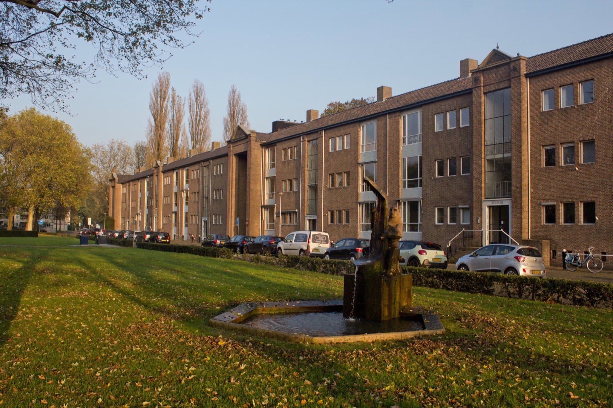 Langgerekt bakstenen woningcomplex van drie lagen aan de Hertog Hendriksingel in 's-Hertogenbosch-Zuid, in laag herfstlicht met een grasveld ervoor.