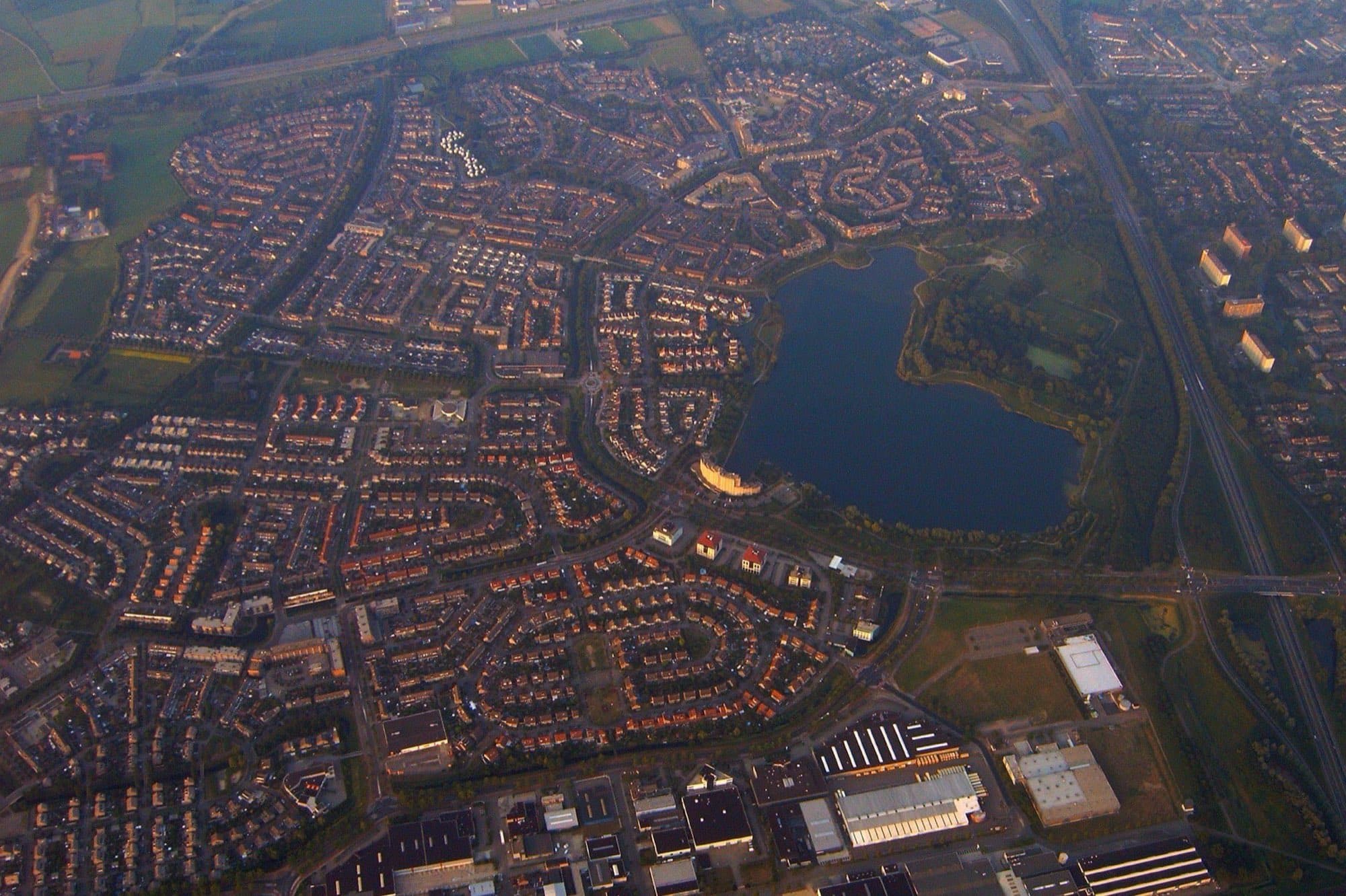 Luchtfoto van de woonwijk Maaspoort in 's-Hertogenbosch met rijtjeswoningen rond een vijver en bedrijfshallen langs de rand.