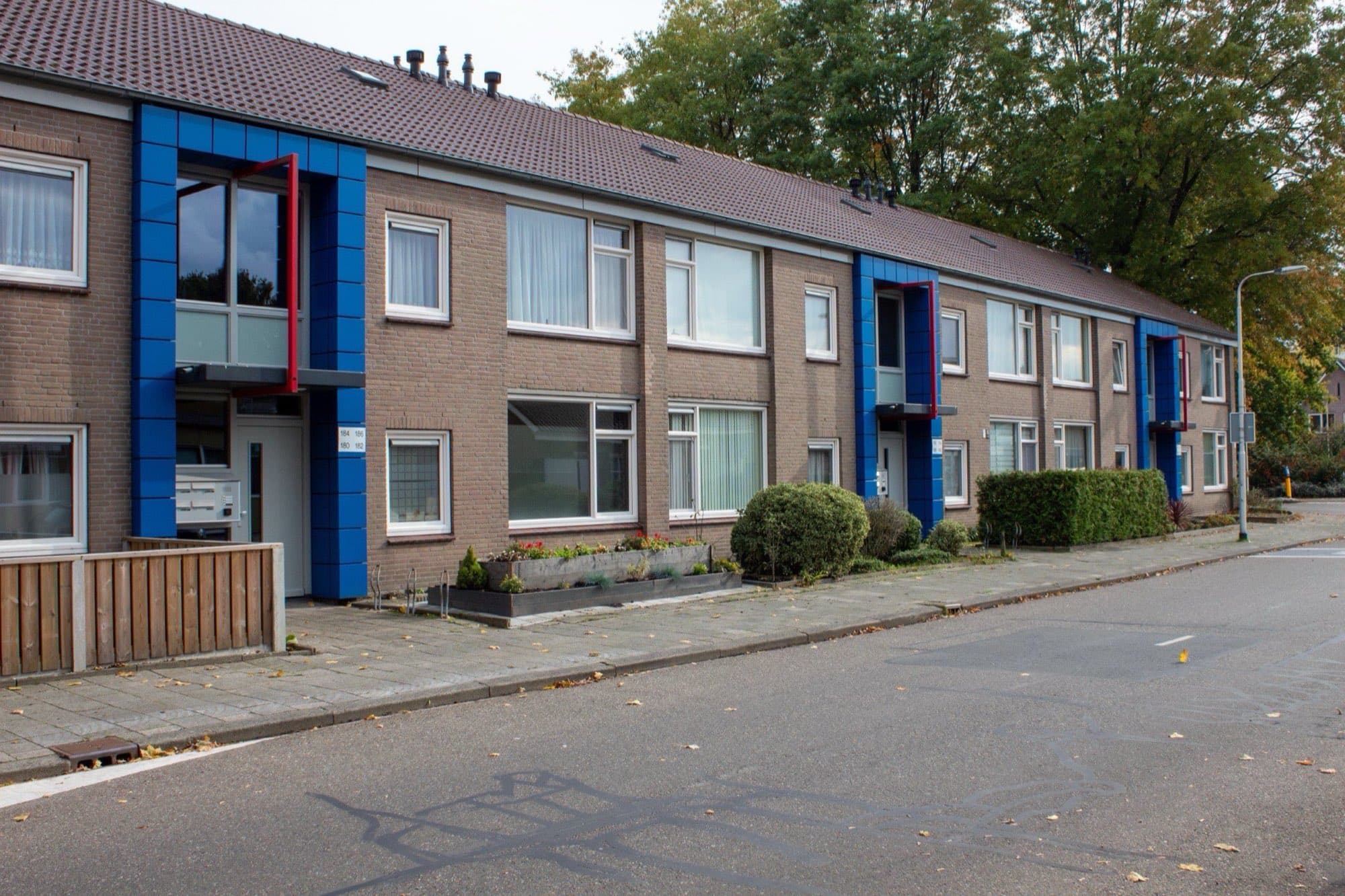 Rij eengezinswoningen in de stijl van de jaren zestig en zeventig, met blauwe accenten en lage heggen, in de wijk Stokhasselt in Tilburg-Noord.
