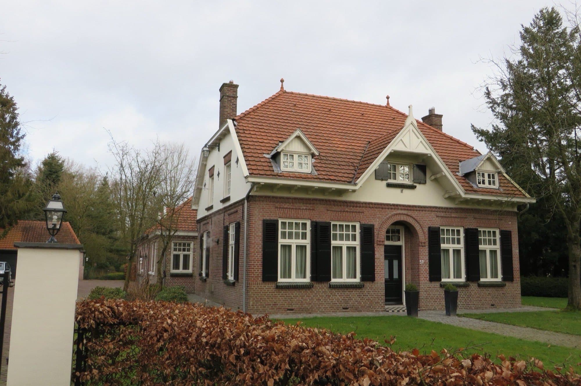 Vrijstaande bakstenen villa uit het begin van de vorige eeuw met rood pannendak, erker en een haag ervoor aan de Dorpsstraat in Valkenswaard.