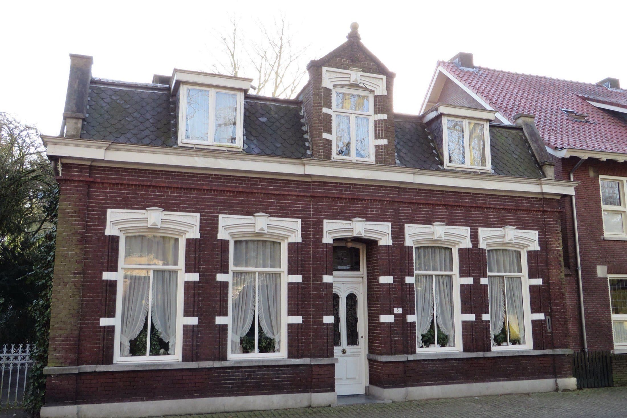 Bakstenen woonhuis met witte sierlijsten rond de ramen, een witte voordeur en dakkapellen in het leien dak aan de Maastrichterweg in Valkenswaard.