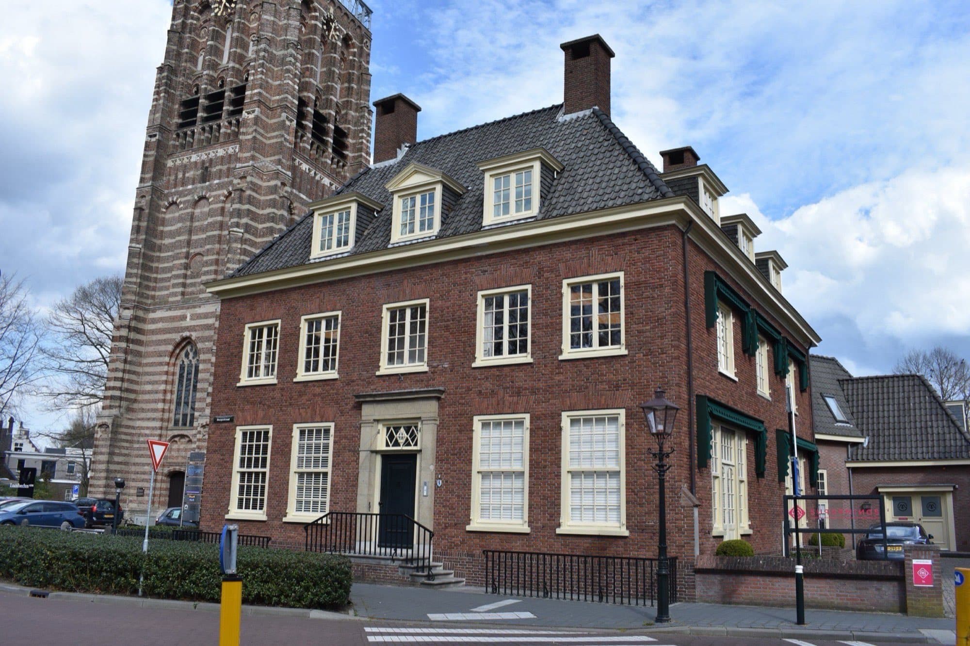 Bakstenen herenhuis met witte kozijnen aan de Dorpsstraat in Vught, met daarachter een kerktoren onder een wolkenlucht.