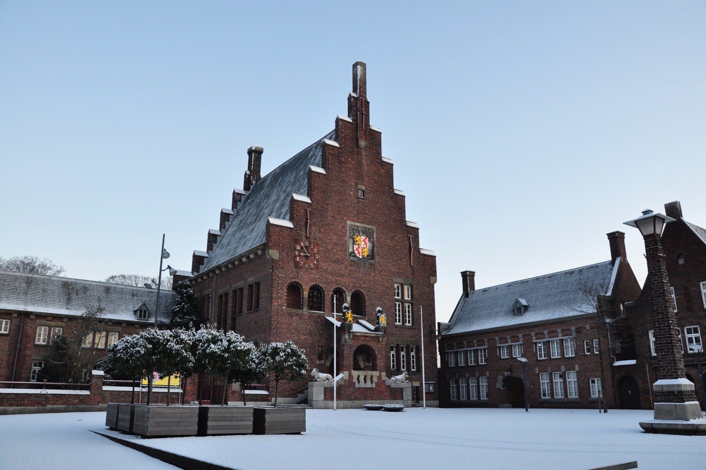 Het oude raadhuis van Waalwijk met trapgevel en klok aan het besneeuwde Raadhuisplein, met bakstenen panden aan weerszijden onder een heldere winterlucht.
